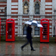 A man shelters under an umbrella as he walks past red telephone boxes in central London April 17, 2012. REUTERS/Olivia Harris (BRITAIN - Tags: CITYSPACE SOCIETY BUSINESS TELECOMS) - RTR30UWV